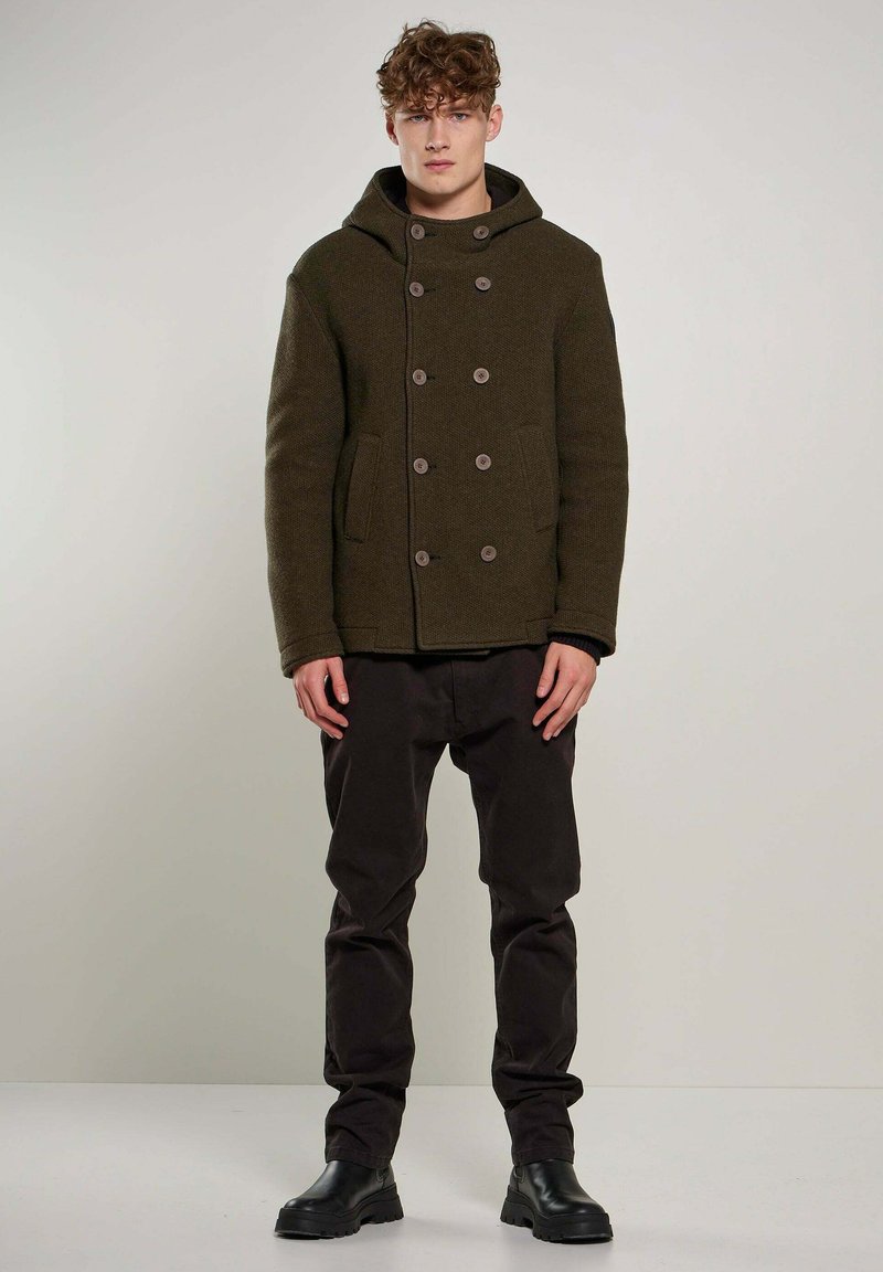 Olijfgroen peacoat met een capuchon, dubbelgeknoopte knopen en zijzakken, gecombineerd met donkere broeken en zwarte gevechtslaarzen.