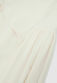 Tessuto color crema con dettaglio di cucitura arricciata, che mostra una texture liscia e morbida e pieghe sottili su materiale leggero.