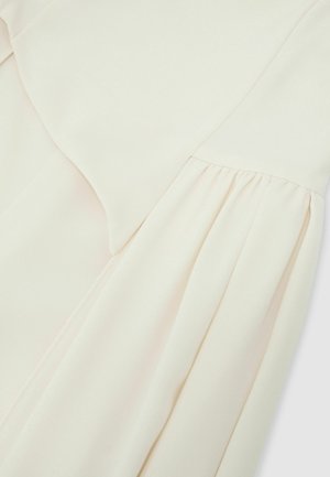 Helekoore värvi kangas kinnitatud õmblusega, mis näitab sujuvat, pehmet tekstuuri ja õrnalt volditud kerge materjali peal.