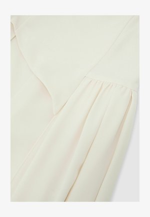 Krēmkrāsas audums ar pīto šuvi, kas parāda gludu, mīkstu tekstūru un smalkas locījumu vieglā materiālā.