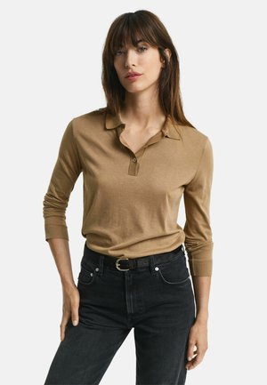 Long-sleeve, light brown polo shirt with a collar and button detail, paired with high-waisted black jeans and a black belt.