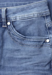 Gros plan sur la poche avant d'un jean en denim bleu avec des coutures visibles, une boucle de ceinture et des rivets en métal.