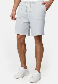 Shorts texturés bleu clair avec taille à cordon, dotés de deux grandes poches latérales et d'une coupe décontractée. Portés avec des chaussures de sport blanches.