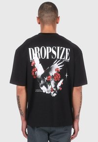 Black cotton t-shirt featuring a large graphic of white birds and red flowers on the back, with "DROPSIZE EST 2020" text above.