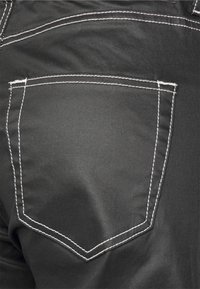 Tecido preto com um bolso traseiro apresentando costura branca contrastante e um brilho sutil. O bolso tem uma forma triangular na parte superior.