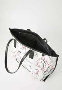 Tote bag in white canvas featuring black leather accents and sketch designs in red and black. Interior includes a zipped pocket.
