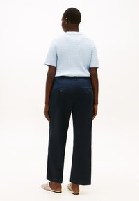 Γαλάζιο υφασμάτινο πουλόβερ με κοντά μανίκια, συνδυασμένο με ναυτικό μπλε παντελόνι φαρδιών ποδιών με πίσω τσέπες, φορεμένο με μπεζ ανοιχτά σανδάλια χωρίς φτέρνα.