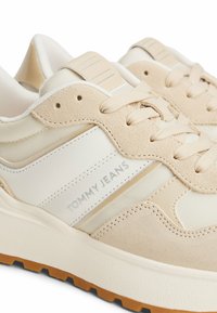 Sneakers beige con un mix di materiali suede e mesh. Le caratteristiche includono un colletto imbottito, lacci tonali e una suola in gomma testurizzata.