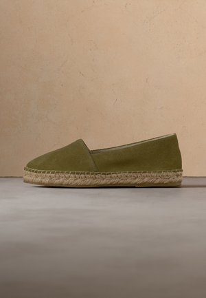 Olivengrøn ruskind espadrille med flettet jutesål, vist i profil mod en beige baggrund.