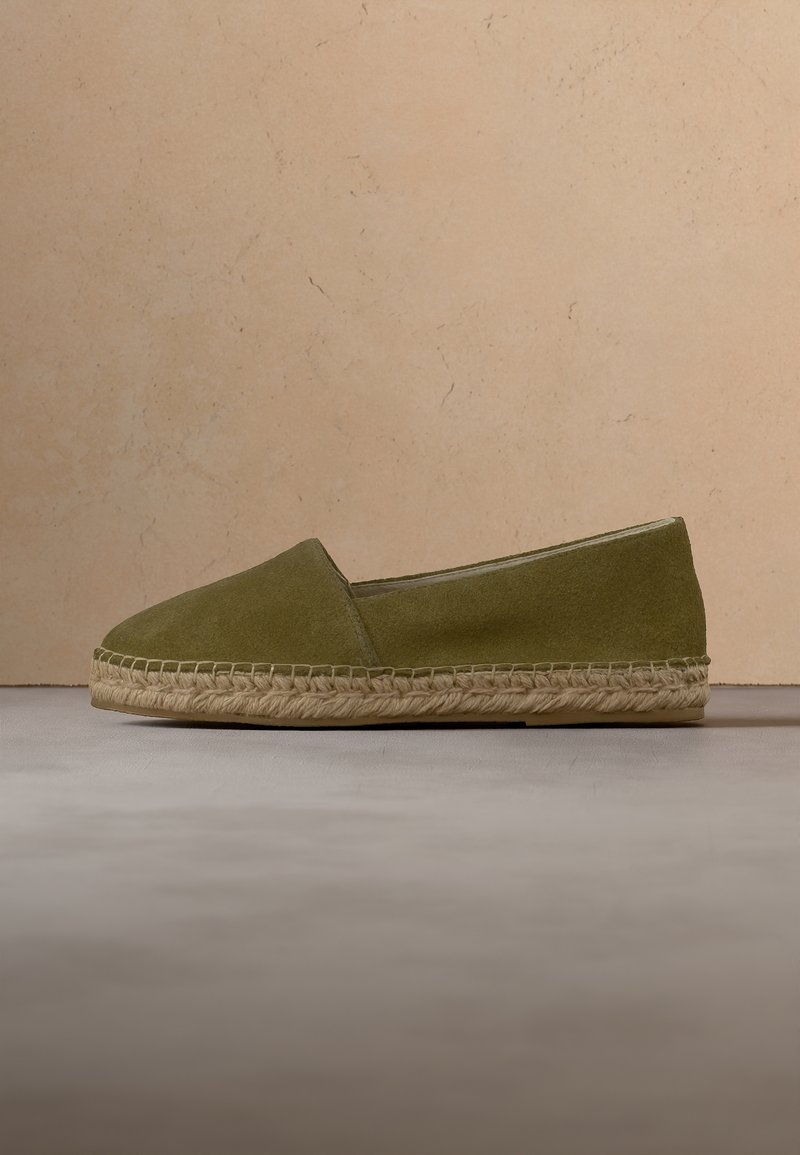 Espadrille en daim vert olive avec une semelle en jute tressée, affichée en profil latéral sur un fond beige.