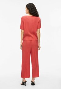 Rode geribbelde twee-delige outfit met korte mouwen en brede pijpen, gemaakt van textuurstof, gecombineerd met zwarte hoge hakken.