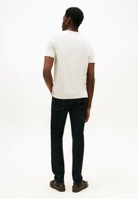 Lys grå kortærmet t-shirt, tætsiddende design, parret med mørkeblå jeans med baglommer og lige pasform, båret med mørke sko.