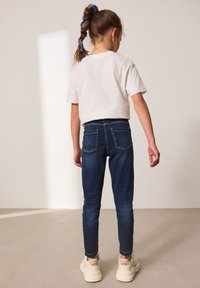 Tamno plave traperice s stražnjim džepovima, uparene s bijelom majicom kratkih rukava. Kosa vezana u rep s svijetloplavim gumicama.