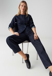 Dunkelblaues Jeanshemd mit Knöpfen, kombiniert mit lockeren dunkelblauen Jeanshosen und schwarzen Schuhen. Glatte Textur, schlichtes Design, legere Passform.