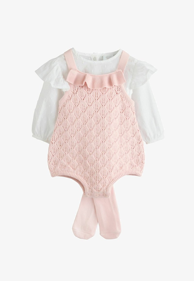 Tutina rosa lavorata a maglia con motivo a rombi in rilievo, abbinata a una camicetta bianca con ruches sotto e calze rosa coordinate.