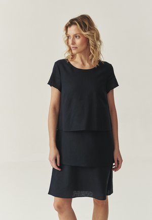 Abito blu navy a strati in lino, con maniche corte e scollo rotondo, con un orlo che cade appena sopra il ginocchio.