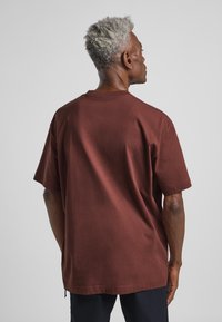 Bruine T-shirt met korte mouwen van katoen, voorzien van een ronde hals en een relaxte pasvorm. De achterkant toont een gladde textuur en geen zichtbare versieringen.
