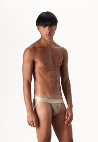 Beige herrunderkläder med en slät tygkonstruktion, låg midja, och en minimalistisk stil med sidoutskärningar och en tjock midjeresår.