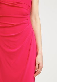 Fuchsia klänning med mjukt, draperat tyg och samlade detaljer på sidan, slät textur och figurnära silhuett som sträcker sig till under knäet.