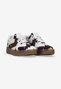 Sneaker con un design a macchie di mucca in bianco e nero, con dettagli in suede marrone, lacci bianchi e una suola in gomma trasparente.