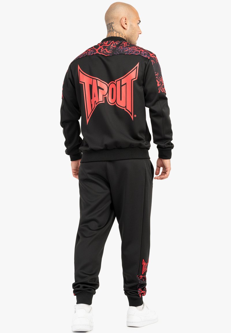 Crni trenirku sa crvenim "TAPOUT" logotipom na leđima. Ima kontrastni uzorak na ramenima i donjim hlačama s elastičnim manžetama i pojasom.