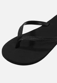 Mustad mustikas flip-flop, millel on mati tallaga, ja läikivad, sädelevad rihmad, mis moodustavad V-kuju jala kohal.