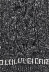 Bonnet en tricot gris foncé présentant un motif en torsades texturé, avec une bande blanche à logo en bas. Matière douce, chaude et élastique.