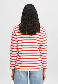 Rot-weißer gestreifter Langarmshirt, Baumwollmaterial, lockere Passform, runder Ausschnitt, sichtbarer Bund, getragen mit hellblauen Jeans.