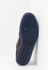 Semelle de basket noire avec une semelle extérieure en caoutchouc bleu texturé. Présente des motifs circulaires et un logo Nike proéminent, avec un accent rouge le long du côté.
