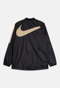 Chaqueta deportiva negra con el logo de Nike en color beige. Cuenta con mangas largas, un cuello alto y material ligero. Textura suave.