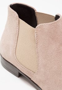 Bottine en daim beige clair avec panneau latéral élastique et petit talon en bois, conçue pour un enfilage facile et un confort optimal.