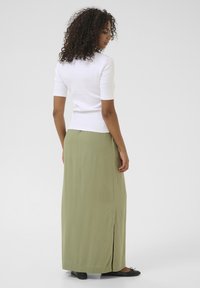 Top bianco a maniche corte abbinato a una lunga gonna verde oliva con uno spacco laterale. La modella indossa delle ballerine nere. Design semplice e minimalista.