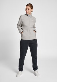 Ljusgrå fleecejacka med hög krage, dragkedja och två sidofickor. Tillsammans med mörka joggers och vita sneakers.