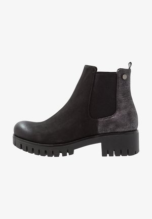 Botín Chelsea negro hasta el tobillo con suela gruesa, panel lateral elástico, parte trasera texturizada y pequeño tirador con detalle de botón metálico.