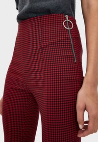 Skräddarsydda byxor i röd och svart hundstooth med dragkedja på sidan och cirkulär dragflik. Strukturerad tyg med rutigt mönster.