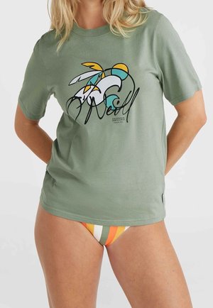 Kobieta nosząca zielony t-shirt z krótkim rękawem z kolorowym abstrakcyjnym wzorem fali i piór oraz pasiastym dołem bikini.