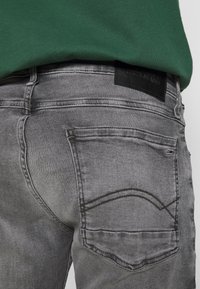 Vaqueros de mezclilla gris con un diseño ajustado, desgaste sutil, doble costura y una etiqueta de cuero en la cinturilla.