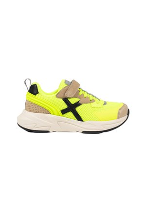 Zapatilla deportiva amarillo neón con detalles beige y negros, parte superior de malla, logo negro, correa beige y suela blanca gruesa con dibujo negro.