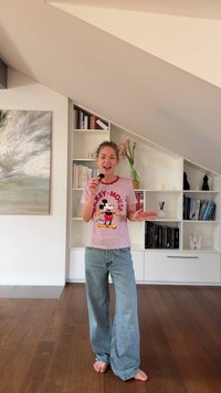 Randig röd och vit t-shirt med en tecknad musdesign, parat med lösa ljusblå jeans; barfota på trägolv.