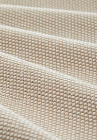 Beige kudotuskangas, jossa on tekstuurinen, ruudukkomainen kuvio, joka sisältää vuorottain vaaleita ja tummia rivejä, lähikuva materiaalista.