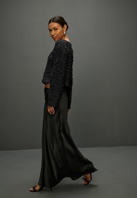 Zwart gestructureerd crop-top met bloemendetails, gecombineerd met een soepel zwart maxi-jurk. De outfit heeft een paar zwarte sandalen met bandjes en eenvoudige oorbellen.