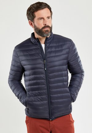 Doudoune marine avec fermeture éclair, design matelassé, col haut et poches latérales. Tissu léger au toucher lisse.