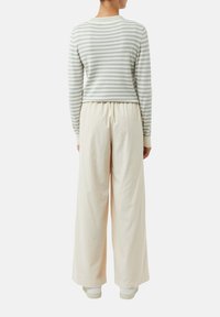 Maglione a righe, verde chiaro e bianco, abbinato a pantaloni a gamba larga color crema, dotati di una fascia elastica in vita e di un tessuto morbido e testurizzato.