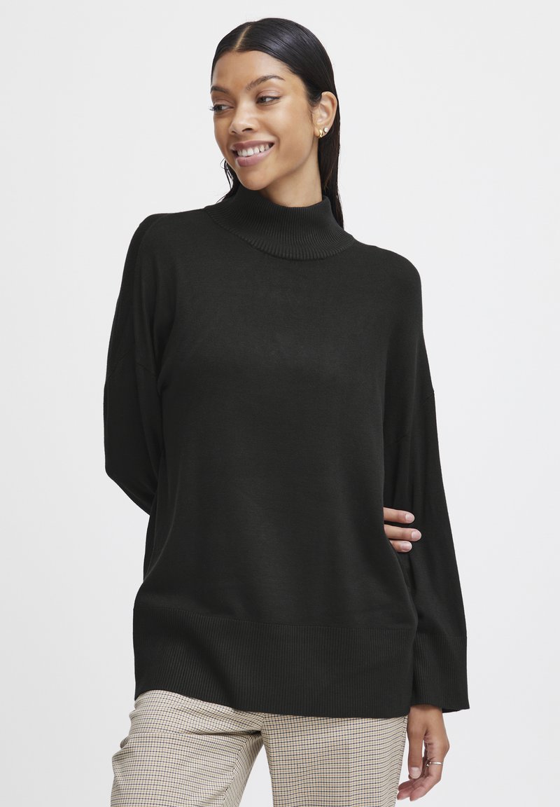 Pulover negru cu guler înalt, cu o croială lejeră și manșete striate, asortat cu o pereche de pantaloni bej cu carouri. Textură moale și design casual.