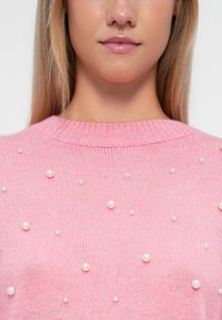 Rosa Strickpullover mit rundem Halsausschnitt und gleichmäßiger Verteilung kleiner dekorativer Perlenakzente auf der Vorderseite.