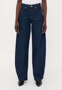 Jeans ampi neri in denim, con vita alta, tasche anteriori e dettagli di cucitura discreti. Abbinati a scarpe nere a punta.