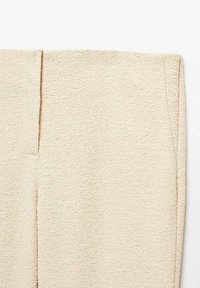 Tissu texturé couleur crème avec une surface légèrement duveteuse, présentant des coutures plates et un bord coupé net, mettant en valeur un design minimaliste.