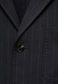 Granatowa marynarka w paski z wyłogowym kołnierzem, zapięciem na guziki i pojedynczą kieszenią na piersi. Teksturowana tkanina z widocznymi detalami szwów.