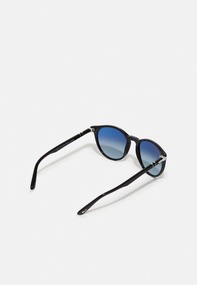Lunettes de soleil noires avec des verres ronds, dotées d'un dégradé bleu. Branches noires fines avec des accents argentés, monture en plastique lisse.