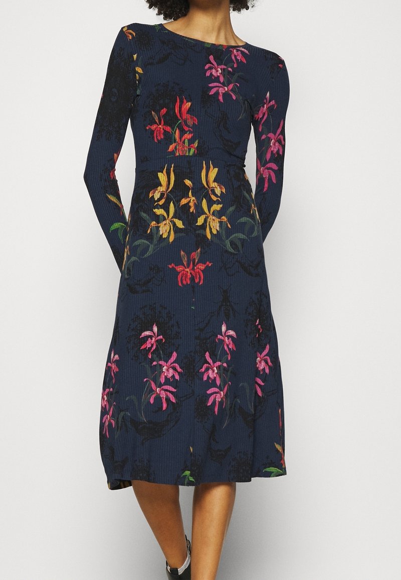 Robe côtelée marine à manches longues, ornée d'imprimés floraux vibrants en rose, jaune et vert. Longueur midi avec une taille cintrée.